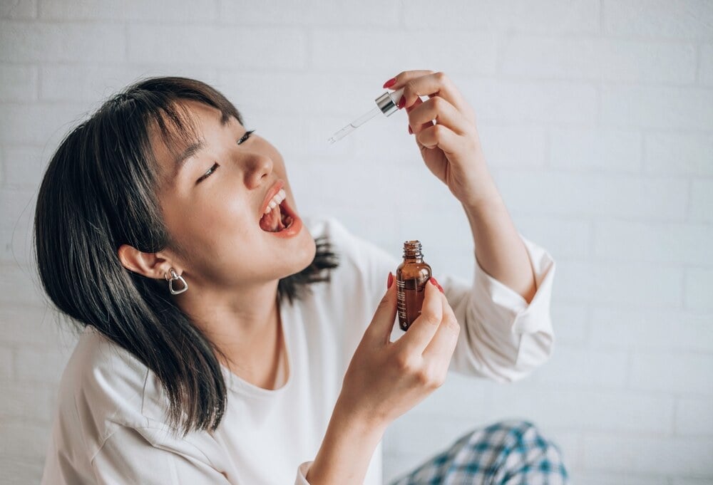 a lady in a white shirt using a tincture to drop thc-p drops under her tongue