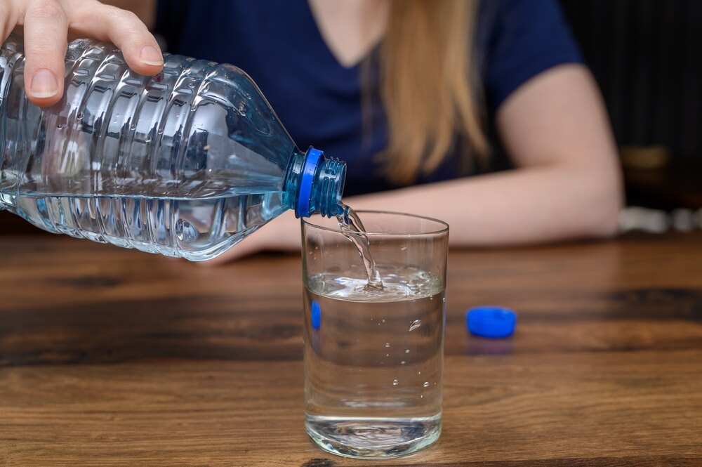 a lady in a blue top pouring a bottle of water into a glass