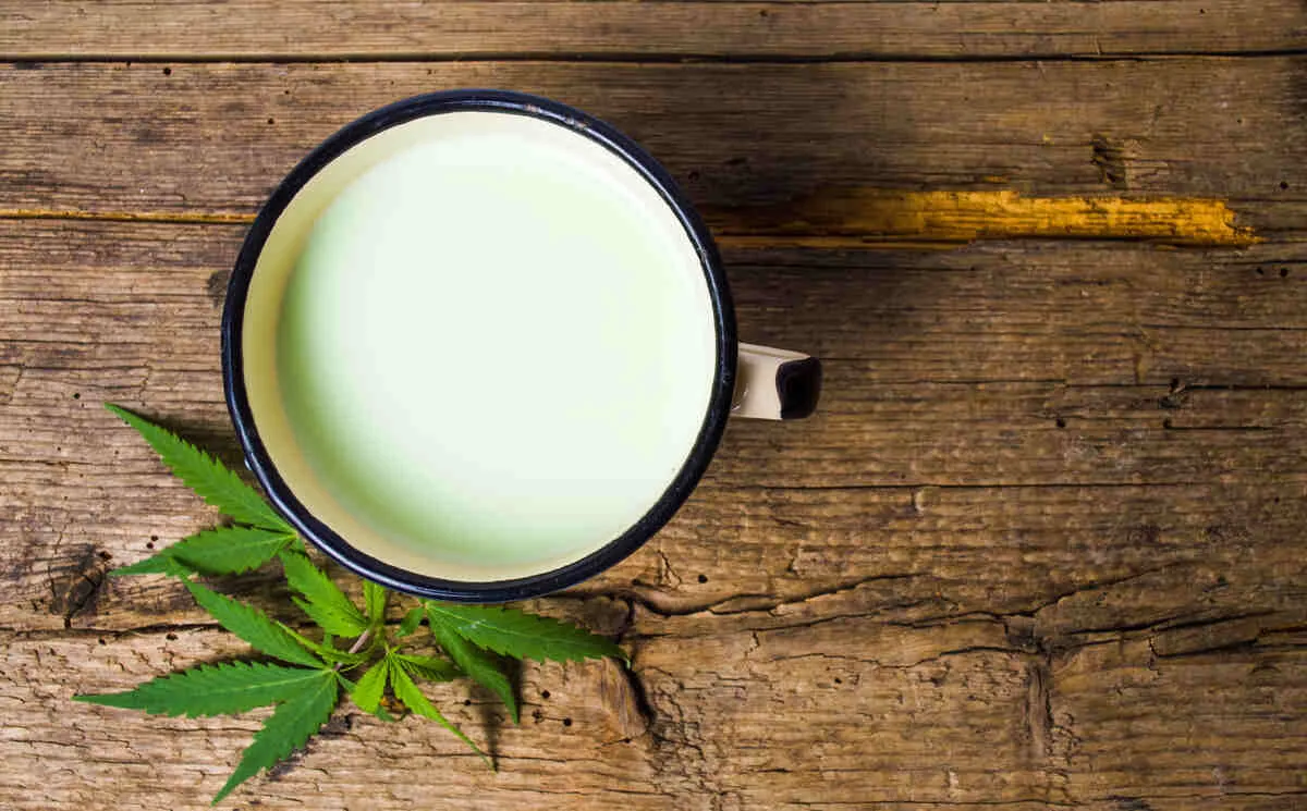 a mug of cannabis milk with a small cannabis leaf next to it on a wooden table