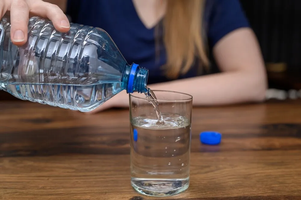 a lady in a blue top pouring a bottle of water into a glass