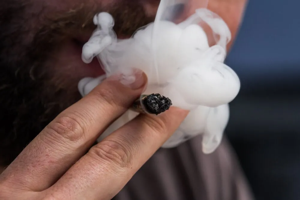 a man smoking weed blowing smoke out of his mouth